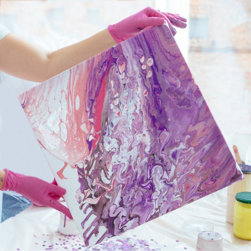 Eine Leinwand mit pinker und Lila Acrylfarbe bemalt wird von einer Dame gehalten