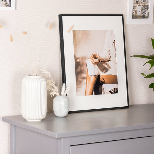 Schwarzer Bilderrahmen Milano aus Aluminium, dekorativ auf Sideboard mit Vasen platziert.