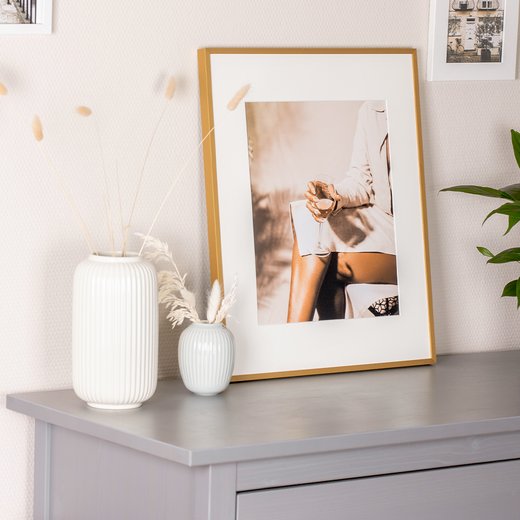 Goldener Bilderrahmen Milano aus Aluminium, dekorativ auf Sideboard mit Vasen platziert.