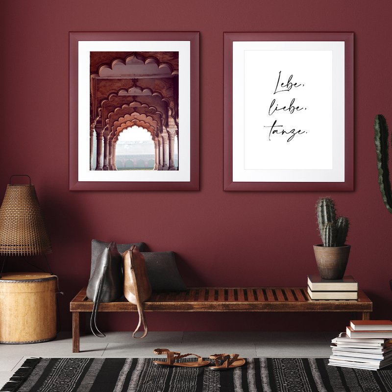 Zwei Pastellrahmen hängen in einem modernen Vorraum an einer matten Dunkelroten Wand mit zwei Kunstdrucken gerahmt. 