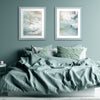Zwei Pastellrahmen hängen in einem modernen Schalfzimmer über einem Bett an einer Pastelltürkisen Wand mit Kunstdrucken vom Meer. 